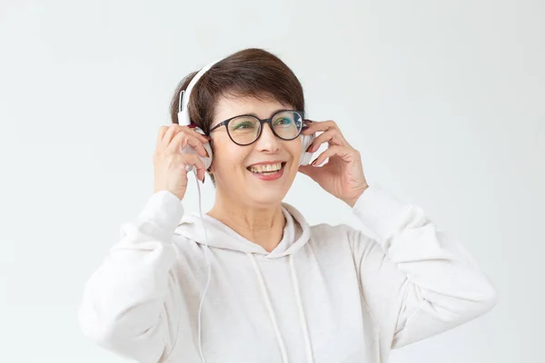 Хобі, інтереси та концепція людей - Красива жінка 40-50 років слухає музику у великих навушниках на білому тлі — стокове фото