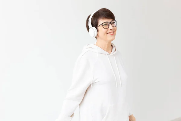Elég lelkes középkorú nő a szemüveg és egy fehér pulóvert hallgat a kedvenc zenéit fejhallgató fehér háttérben a másolási hely. Online rádió-és zeneelőfizetési koncepció. — Stock Fotó