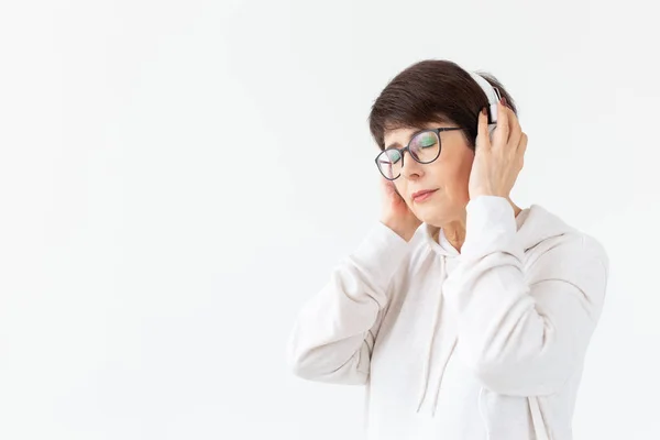 Beautiful woman 40-50 years old listening music in big headphone on white background with copy space — Stock Photo, Image