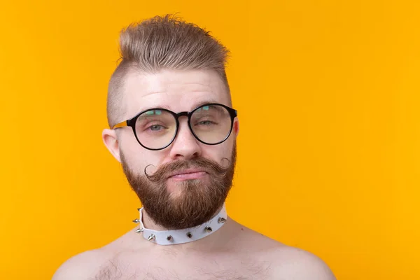 Joven hombre de moda positivo hipster con una barba bigote y collar fetiche en camisa posando sobre un fondo amarillo. Concepto de roca y subcultura . —  Fotos de Stock