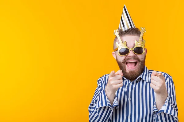 Joven hipster alegre macho con una gorra de papel y gafas se ríe felizmente sobre un fondo amarillo con espacio para copiar. El concepto de una mega fiesta y vacaciones . — Foto de Stock