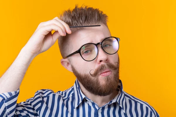 Retrato de un joven hipster guapo divertido con bigote y barba peinándose el pelo sobre un fondo amarillo. Concepto de barbería y autocuidado . — Foto de Stock