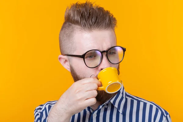 Lindo joven confiado bebiendo café de una taza amarilla mientras está de pie sobre un fondo amarillo. Concepto de café de la mañana o espresso . — Foto de Stock