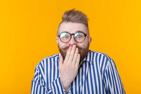 Überrascht junge männliche Hipster mit Brille verlegen den Mund bedeckt und lacht posierend auf gelbem Hintergrund. Konzept der Zeichnung und Überraschung. — Stockfoto