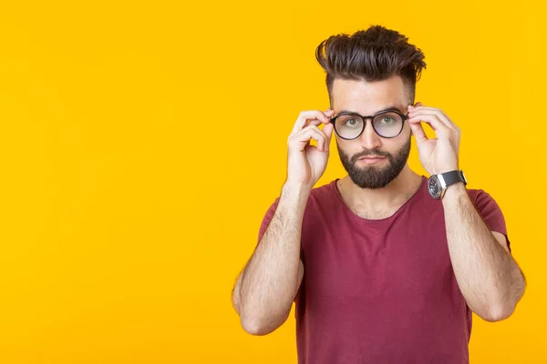 Joven chico guapo está mirando sus gafas mientras está de pie sobre un fondo amarillo. El concepto de mala visión y tratamiento ocular . — Foto de Stock
