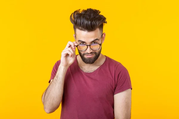 Retrato de un guapo joven hipster con gafas y barba mirando pensativamente a la cámara sobre un fondo amarillo. Concepto de elección y publicidad — Foto de Stock