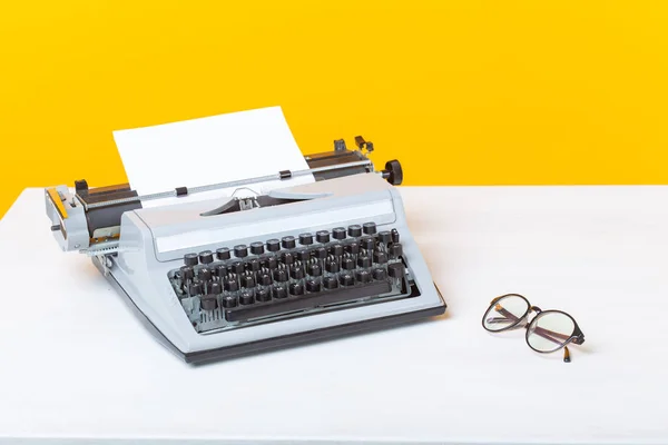 Lugar de trabajo del gerente de la secretaria y la máquina de escribir de negocios y gafas están sobre la mesa sobre un fondo amarillo. Concepto de trabajo . — Foto de Stock