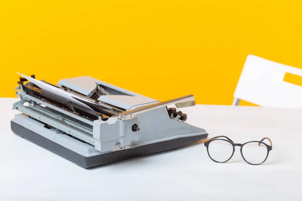 Ο χώρος εργασίας του διευθυντή του γραμματέα και της επιχειρηματικής γραφομηχανή και των γυαλιών είναι στο τραπέζι σε κίτρινο φόντο. Ιδέα εργασίας γραφείου. — Φωτογραφία Αρχείου