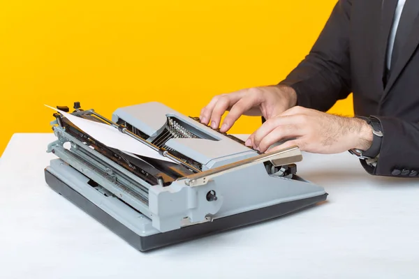 Lukning af forretningsmand eller leder i formelt jakkesæt skrive tekst på en skrivemaskine på en gul baggrund. Begrebet forretnings- og kontorarbejde - Stock-foto