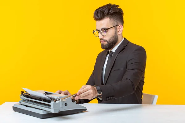 Joven hombre de negocios guapo en ropa formal escribiendo texto en una máquina de escribir posando sobre un fondo amarillo. Lugar para la publicidad. Concepto empresarial . — Foto de Stock