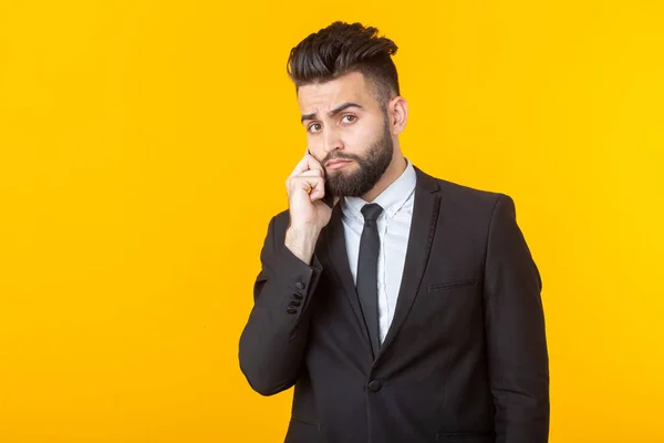 Cute young man with a beard in formal clothes talking on the phone posing on a yellow background. Concept of an informal meeting and business deal.