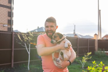 Sakallı pozitif genç adam sevgili köpeği Jack Russell Terrier tutuyor ve güneşli bir yaz gününde onun kır evinin bahçesinde ortak bir dinlenme tadını çıkarıyor. Onların dört için aşk kavramı