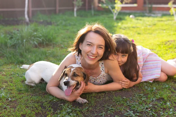 Une jeune mère, une fille et un chien positifs sont allongés sur la pelouse de leur maison de campagne et profitent d'un repos conjoint pendant le week-end par temps chaud — Photo