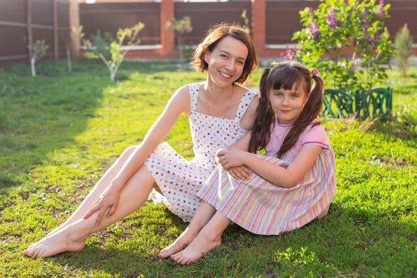 Menina em vestido rosa com sua mãe no quintal sentado na grama — Fotografia de Stock