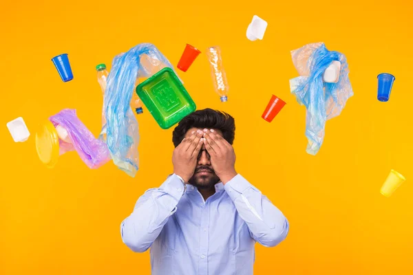 Plastic recycling problem, ecology and environmental disaster concept - Indian man closed his eyes with hands on yellow background. He is terrified by trash problems