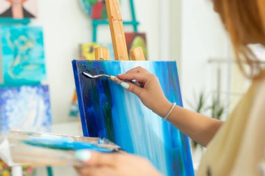 Sanat sınıfı, çizim ve yaratıcılık konsepti - Palet ve boya fırçası ile şövale önünde oturan kız öğrenci, yakın çekim