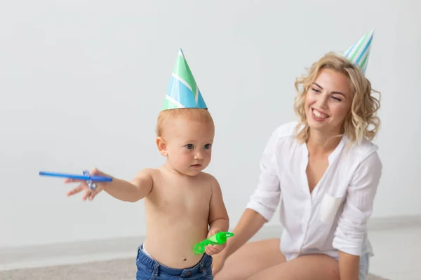 Joven madre sonriente y linda hijita en gorras de cumpleaños pasando tiempo juntos en la alfombra en casa. Vacaciones familiares y valores — Foto de Stock
