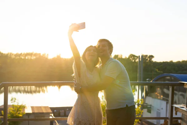 Casal romântico engraçado bonito no fundo da natureza. Jovem atraente e homem bonito estão fazendo selfie, sorrindo e olhando para a câmera . — Fotografia de Stock