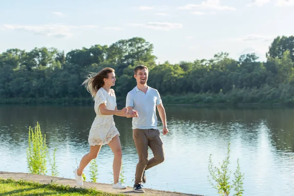 Conceito de amor e relacionamento - O homem e mulher feliz correndo em um parque perto de um lago — Fotografia de Stock