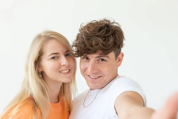 Charmig ungt par Söt blond flicka flicka ta en selfie poserar över vit bakgrund. Koncept ett ungt par tonåringar eller Millennials i kärlek. — Stockfoto