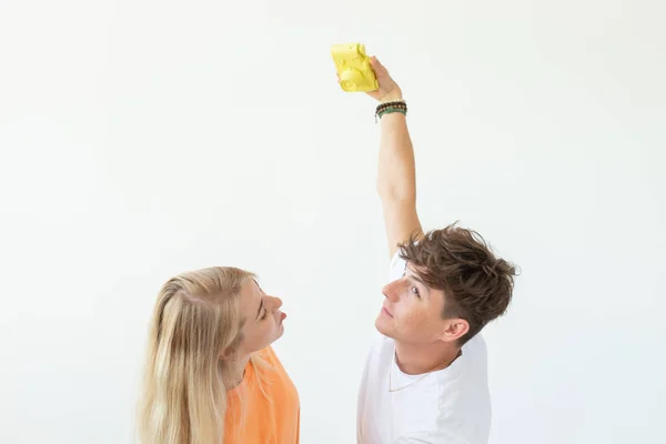 Drôle de jeune fille blonde couple fou et un gars hipster prendre un selfie sur une caméra de film jaune vintage posant sur un fond blanc. Concept de passe-temps de photographie . — Photo