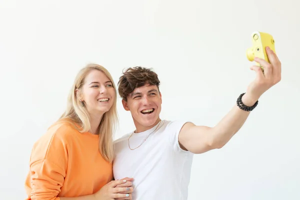 Lustiges junges verliebtes Paar, netter Mann und charmante Frau, die ein Selfie auf einer gelben Filmkamera machen, die auf weißem Hintergrund posiert. Liebhaber von Fotografie und Hobbys. — Stockfoto