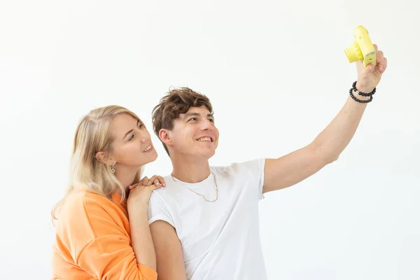 Lustiges junges verliebtes Paar, netter Mann und charmante Frau, die ein Selfie auf einer gelben Filmkamera machen, die auf weißem Hintergrund posiert. Liebhaber von Fotografie und Hobbys. — Stockfoto