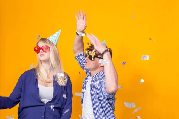 Festa, feriado e conceito de aniversário - Jovem casal engraçado dançando de pé contra fundo amarelo com confete — Fotografia de Stock