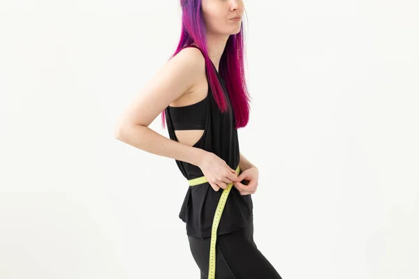 Unbekannte junge Hipsterin mit lila Haaren misst ihre Taille mit einem Maßband auf weißem Hintergrund. gesunder Lebensstil. Werbefläche. — Stockfoto