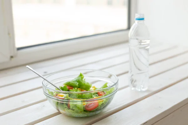La salade de légumes et la bouteille d'eau reposent sur un rebord de fenêtre blanc. Concept d'un mode de vie sain activité physique et bonne alimentation . — Photo