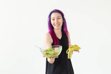 Genç asyalı kız hipster renkli saç elinde bir ölçüm bant ve sebze salatası copyspace ile beyaz bir arka plan üzerinde poz tutarak. Sağlıklı beslenme konsepti.