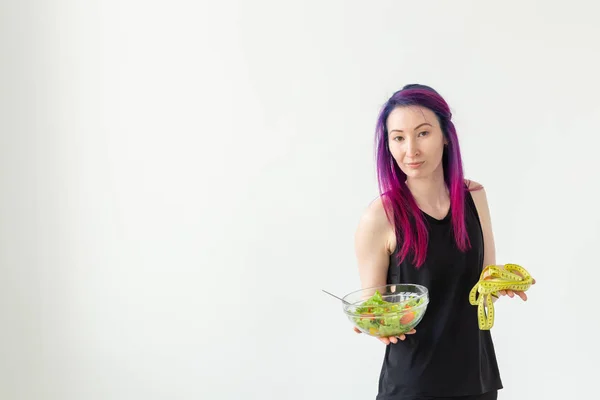 Молодая блоггерша фитнес держит овощной салат и измерительную ленту. Концепция спортивного образа жизни и правильного питания. Белый фон с копировальным пространством — стоковое фото