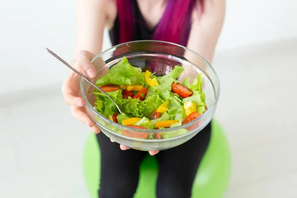 Close-up of young fitness girl holding vegetable salad. Concept of sports lifestyle and proper nutrition.