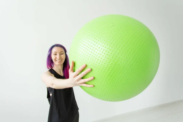 Niña alegre positiva borrosa hipster sosteniendo una pelota verde en sus brazos durante las clases en el gimnasio. Concepto de yoga y pilates y fitness . — Foto de Stock