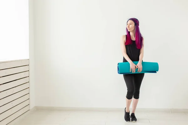 Junges nettes Mädchen Hipster mit farbigen Haaren hält in der Hand eine Sportmatte posiert auf einem weißen Klassenhintergrund. gesunder Lebensstil und Fitness-Konzept — Stockfoto