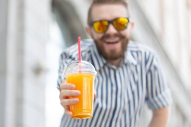 Elinde taze portakal suyu tutan sakallı ve bıyıklı bulanık ve şık genç hipster erkek portresi. Sağlıklı atıştırmalık konsepti.