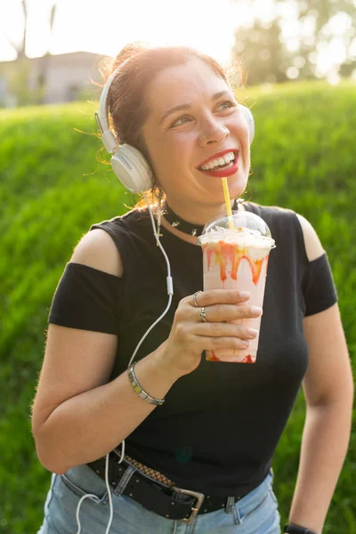 Портрет позитивної молодої красивої дівчини в панк-одязі і окулярах з молочним коктейлем в її руках позує в літньому парку в теплий літній вечір. Концепція відпустки . — стокове фото