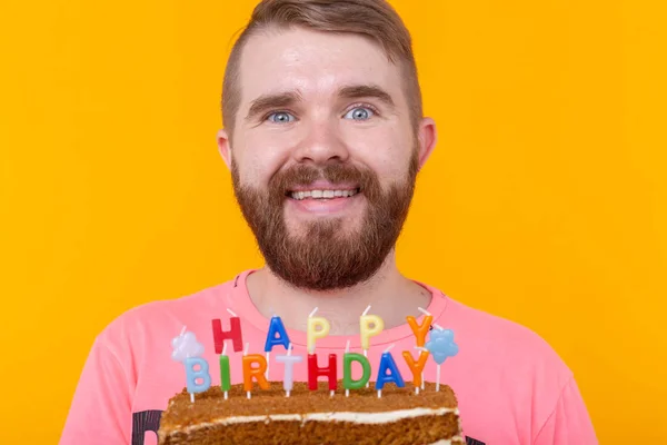 Crazy funny positive guy Hipster mit einem Happy Birthday Kuchen in den Händen steht auf einem gelben Hintergrund. Konzept der Witze und Urlaubsgrüße. — Stockfoto