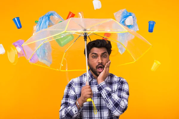 Problema de lixo, reciclagem de plástico, poluição e conceito ambiental - Homem indiano surpreso pensando sobre ecologia sob guarda-chuva em fundo amarelo — Fotografia de Stock