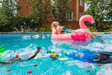 Çöp sorunu, plastik geri dönüşüm, kirlilik ve çevre kavramı - aptal kadın yüzer ve kirli bir havuzda eğlenin. Şişeler ve plastik torbalar onun yanında yüzer.