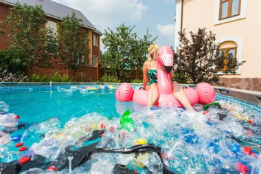 Çöp sorunu, plastik geri dönüşüm, kirlilik ve çevre kavramı - aptal kadın yüzer ve kirli bir havuzda eğlenin. Şişeler ve plastik torbalar onun yanında yüzer.