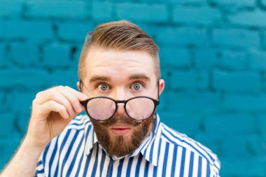 Mavi bulanık tuğla duvar bir arka plan üzerinde poz bıyık lı ve sakallı meraklı bir sürpriz genç adamın yakın çekim portresi. Sürpriz ve şok edici bilgi kavramı.