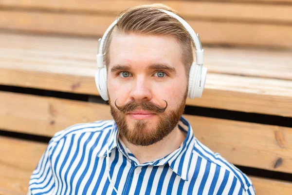 Retrato de cerca de un joven estudiante serio escuchando su radio en línea favorita usando auriculares mientras está sentado en un parque en un día soleado y cálido de verano. . — Foto de Stock