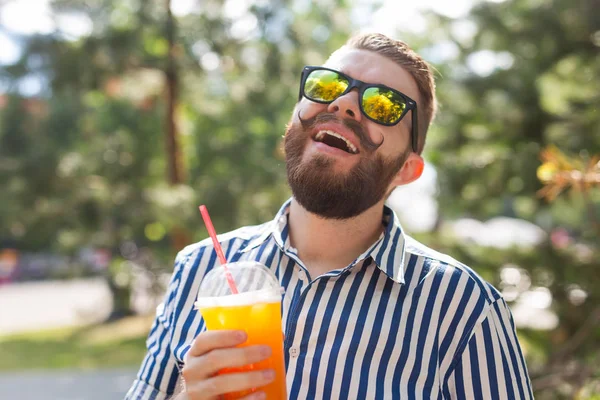 Retrato de un joven positivo y alegre con un vaso de jugo con una pajita mientras camina por el parque en un cálido día soleado de verano. El concepto de descanso después del estudio y el trabajo los fines de semana . — Foto de Stock