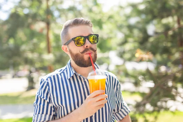 Portret van een positieve vrolijke jongeman met een glas sap met een rietje tijdens het wandelen in het Park op een warme zonnige zomerdag. Het concept van rust na studie en werk in het weekend. — Stockfoto