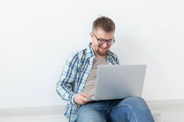 Pozytywny młody człowiek w casual ubrania i okulary surfowania po Internecie za pomocą Wi-Fi i laptopa w poszukiwaniu mieszkań wynajmu. Koncepcja houseocieplenia i wyszukiwania mieszkania. — Zdjęcie stockowe