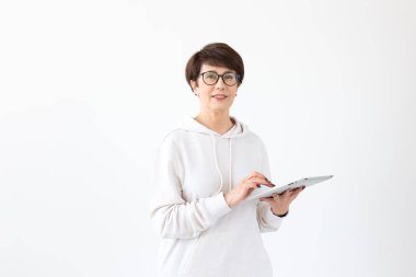 Rahat giysiler içinde Sevimli orta yaşlı kadın beyaz bir arka plan üzerinde bir tablet kullanarak online mağazalar arıyor. Kablosuz internet ve online alışveriş kavramı. Copyspace.