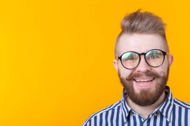 Kopya alanı ile sarı bir arka planda poz gömlek bıyık sakal ve fetiş kolye ile genç pozitif trendy adam hipster. Rock ve alt kültür konsepti.