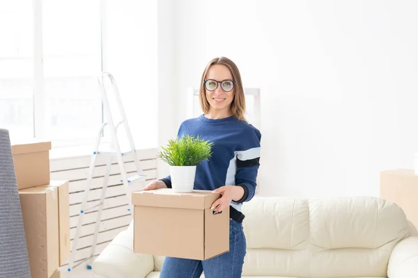 Jonge vrouw houdt een doos en een pot van planten tijdens het verhuizen naar een nieuw appartement. Inwijdingsfeest en nieuw huisvestings concept. — Stockfoto