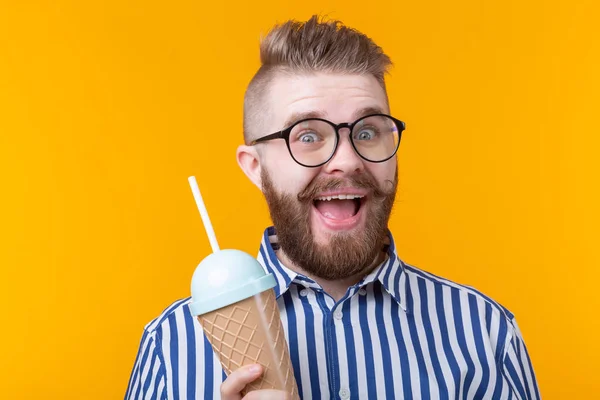 Hipster joyful crazy young guy holding a cocktail in his hands with a straw tube posing on a yellow background. Concept of cafes and restaurants.